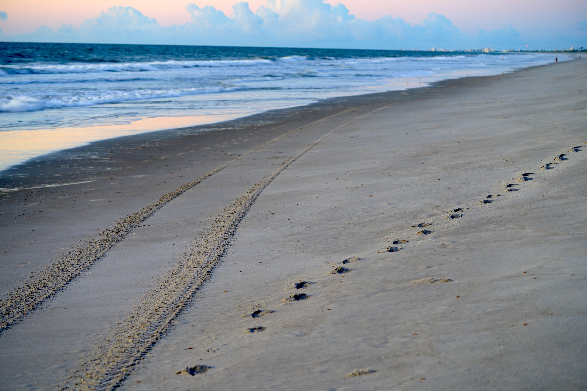 Converging footprints and tire tracks in Cocoa Beach sand at sunset